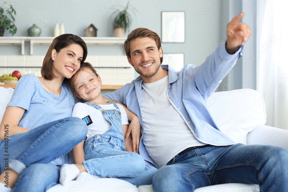 Happy family with child sitting on sofa watching tv, young parents embracing daughter relaxing on couch together. Happy family with child sitting on sofa watching tv, young parents embracing daughter relaxing on couch together.