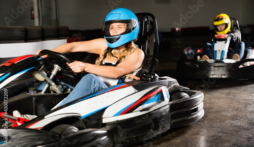 Glad cheerful positive smiling girl and her friends competing on racing cars at kart circuit