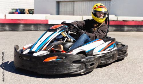 Young female in helmet driving car for karting in sport club outdoor © JackF
