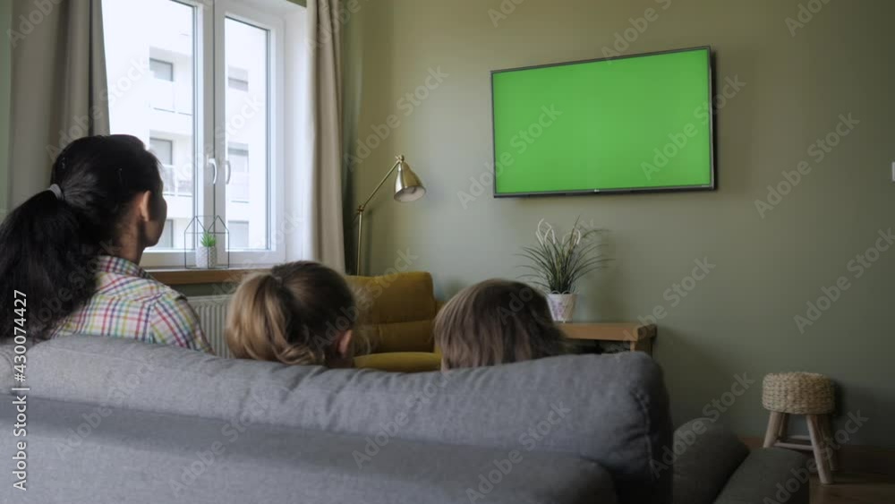 Family Sitting Together Sofa In Their Living Room Watching TV Green Screen. Rear View Of Family With Children Sitting On Sofa In Living Room Day Watching Green Mock-up Screen TV Together. Family Sitting Together Sofa In Their Living Room Watching TV Green Screen. Rear View Of Family With Children Sitting On Sofa In Living Room Day Watching Green Mock-up Screen TV Together.