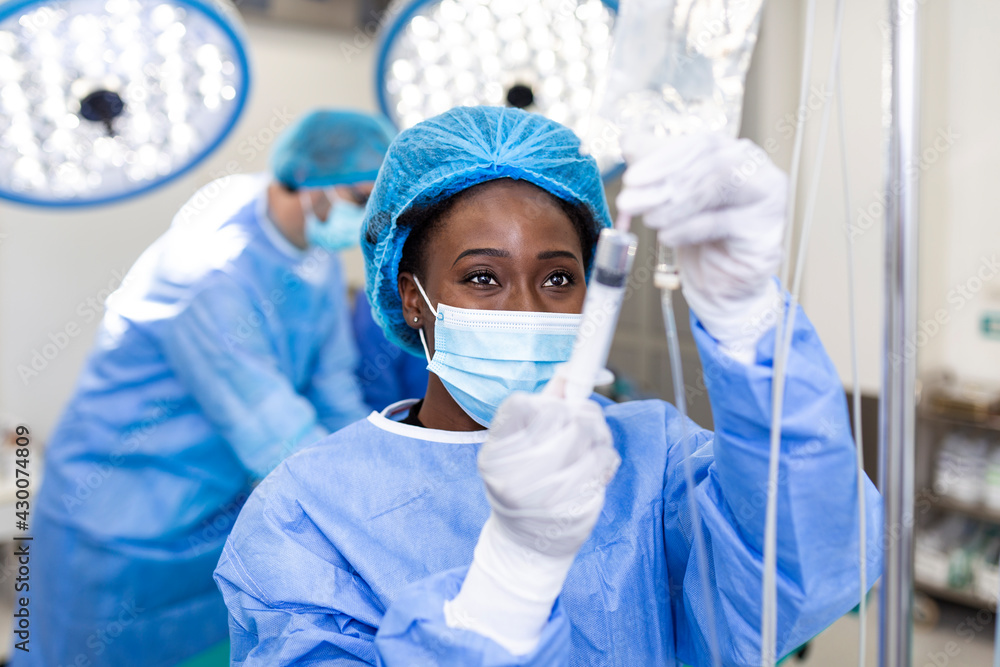 African american female Doctor in the operating room putting drugs through an IV - surgery concepts African american female Doctor in the operating room putting drugs through an IV - surgery concepts