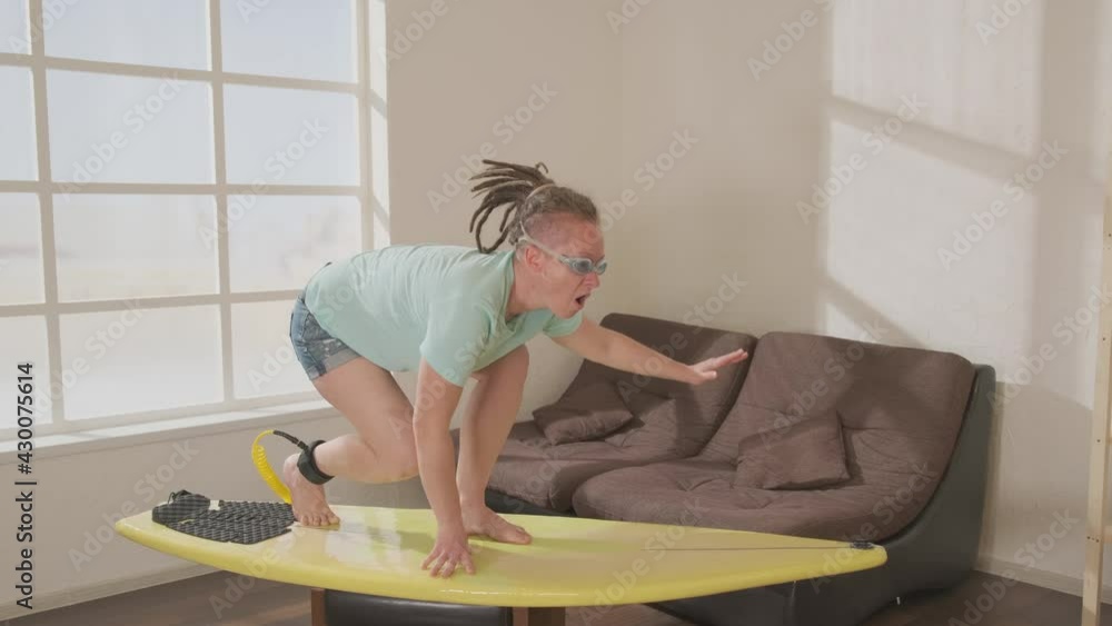 Female surfer practicing on surfboard in living room when spending on vacation at home during lockdown. Fun video. Female surfer practicing on surfboard in living room when spending on vacation at home during lockdown. Fun video.
