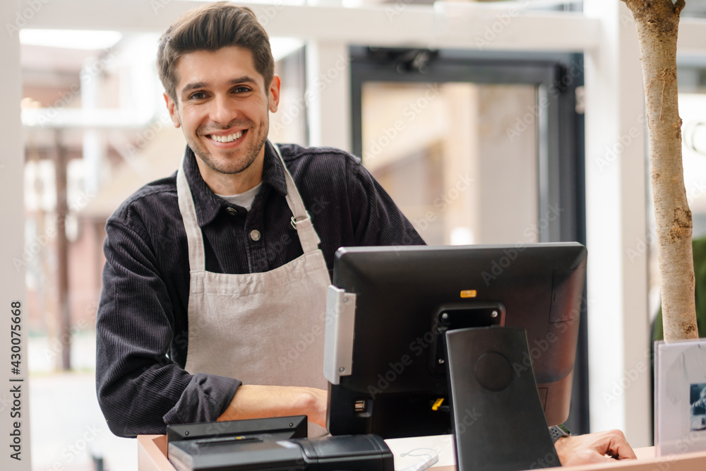 © Drobot Dean - Smiling young man in apron standing at the cash register © Drobot Dean - Smiling young man in apron standing at the cash register
