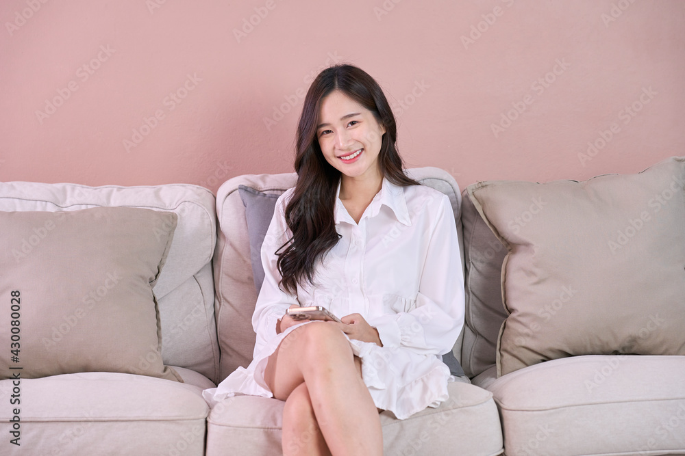 Attractive woman wear white dress use phone while sitting on sofa and smile Attractive woman wear white dress use phone while sitting on sofa and smile