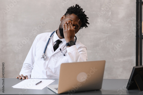 Funny bored at work african american doctor worker falling asleep at office desk, employee sleeping at workplace near laptop feel overworked concept