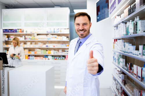 Portrait of smiling caucasian pharmacist standing in drug store with thumbs up.
