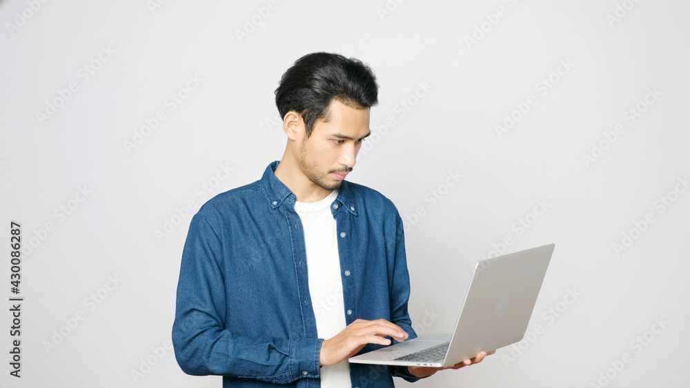 Young asian man holding laptop computer standing on isolated grey background, people and technology Young asian man holding laptop computer standing on isolated grey background, people and technology
