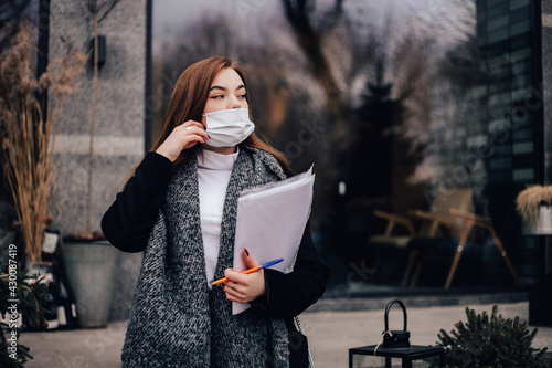 Small busy business owner elegant pretty woman office manager freelancer sitting outside street cafe coffee shop, signing documents, working with papers. Entrepreneur face blue disposable mask