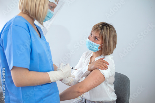 Female doctor holding syringe making covid 19 vaccination injection dose in shoulder of female patient wearing mask. Flu influenza vaccine clinical trials concept  corona virus treatment