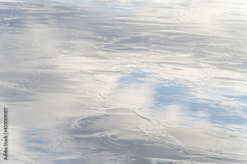 Part of a shiny, frozen lake, with reflection of the blue cloudy sky. Background, backdrop