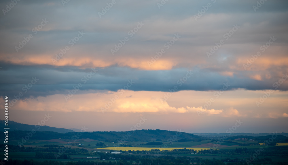 Soft glow of sunset reflects in clouds, last light picks out a distant field of golden mustard in this view over an Oregon valley filled with farm fields. 