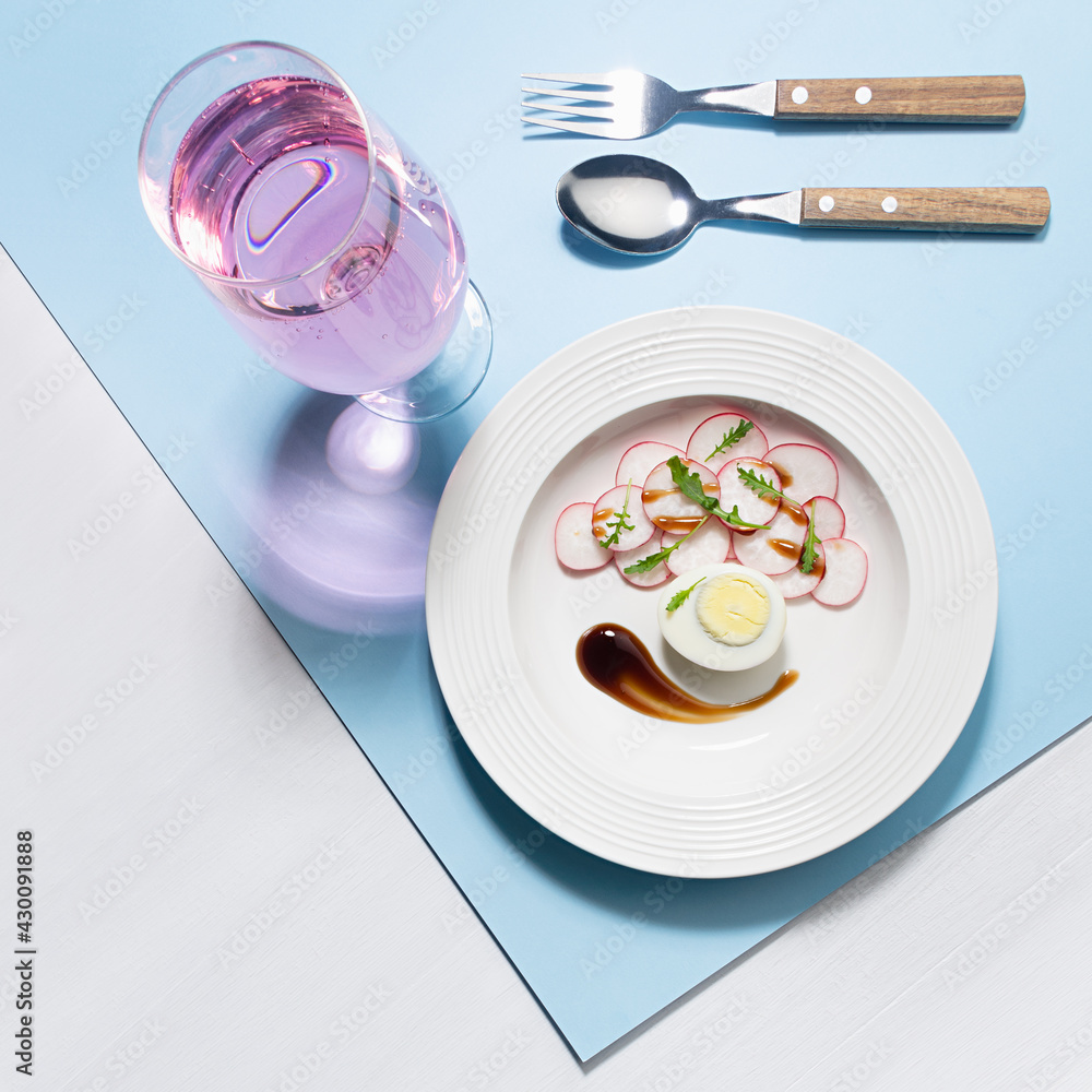 Healthy lifestyle and eating - spring salad of raw fresh vegetables - radish, arugula with eggs, balsamic sauce and rose wine in sunlight with shadow, top view, on white wooden table, blue background. Healthy lifestyle and eating - spring salad of raw fresh vegetables - radish, arugula with eggs, balsamic sauce and rose wine in sunlight with shadow, top view, on white wooden table, blue background.