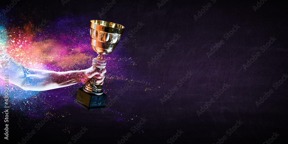 Fototapeta premium Hand holding up a gold trophy cup against dark background