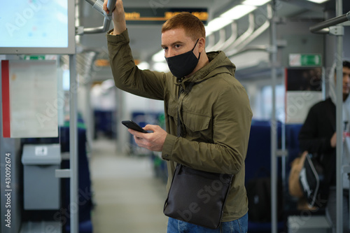 Handsome guy in respirator. man using his smartphone while traveling on the subway. He is wearing a medical mask.