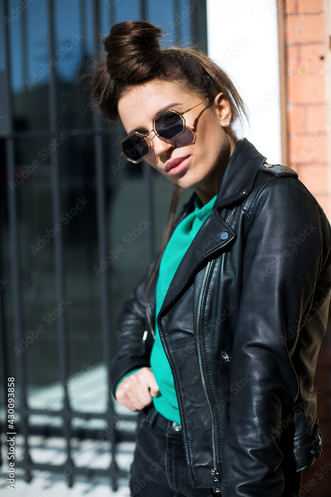 female in black leather jacket, shorts and fashionable sunglasses staying on the stairs near closed shop
