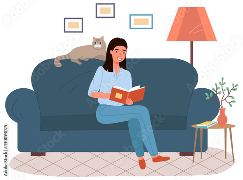Young woman is sitting on couch and reading book. Lady studying textbook. Person spends time and rests in apartment with paper book and big cat. Female pet owner is reading literature at home