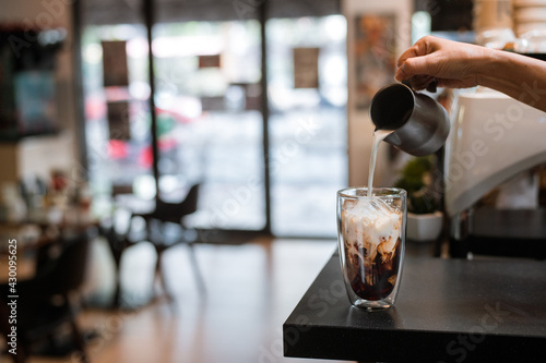 Barista pouring milk into a glass of iced coffee