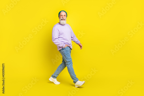 Full length body size photo of smiling elder man wearing stylish clothes going forward isolated on bright yellow color background