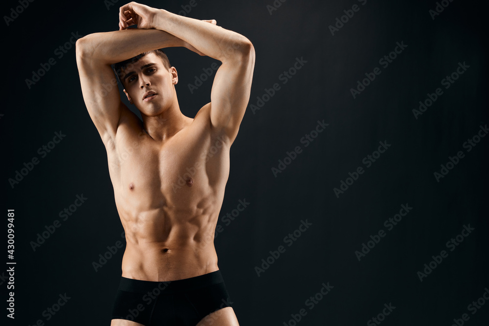 a handsome man with a pumped-up body holding his hands above his head Against a dark background a handsome man with a pumped-up body holding his hands above his head Against a dark background