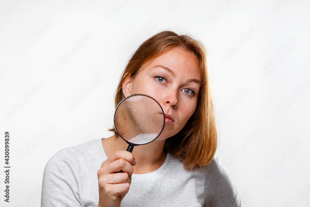 Portrait of a young woman holding a magnifying glass to her face. White background. The concept of search, research and business Portrait of a young woman holding a magnifying glass to her face. White background. The concept of search, research and business