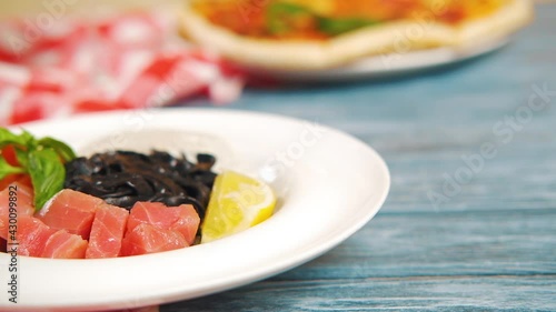 Wallpaper Mural Black cuttlefish ink pasta with salmon fish, lemon, basil in a white plate on wooden table. Served with a glass of white wine. Camera moving slowly over dish. Close-up, high quality. Torontodigital.ca
