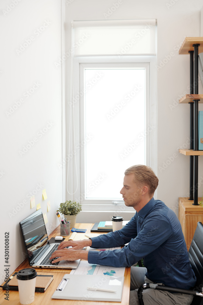 Young businessman working on laptop at office table, analyzing financial charts and filling report document Young businessman working on laptop at office table, analyzing financial charts and filling report document