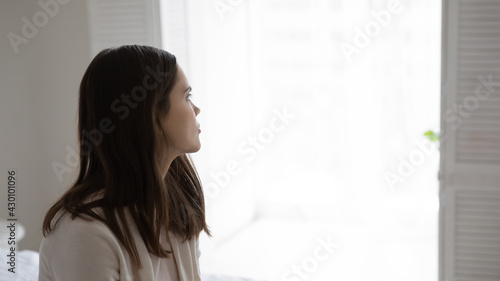 Thoughtful millennial young woman looking away at window at home. Pensive teenage girl lost in thoughts thinking over problem solving, feeling sad, frustrated, lonely, depressed. Copy space