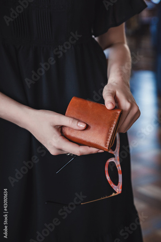 The woman is holding a brown leather wallet and sunglasses. Close-up, no face, vertical orientation, copy space.