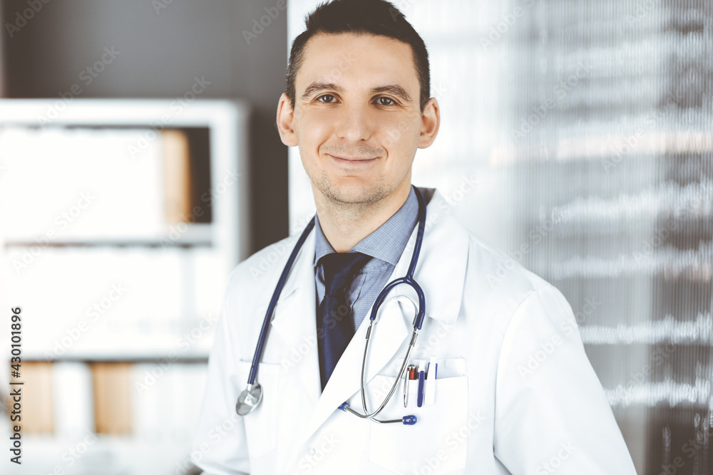 Male doctor standing straight in clinic near his working place. Perfect medical service in hospital. Medicine and healthcare concept Male doctor standing straight in clinic near his working place. Perfect medical service in hospital. Medicine and healthcare concept