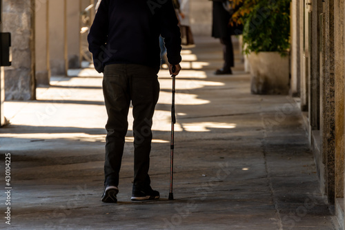 Fototapeta Old man walking alone with a cane along a street.