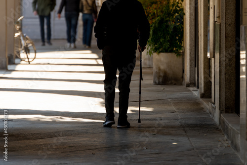 Old man walking alone with a cane along a street.  © leledaniele