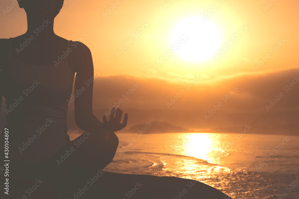 Woman doing yoga exercise on seashore at sunset