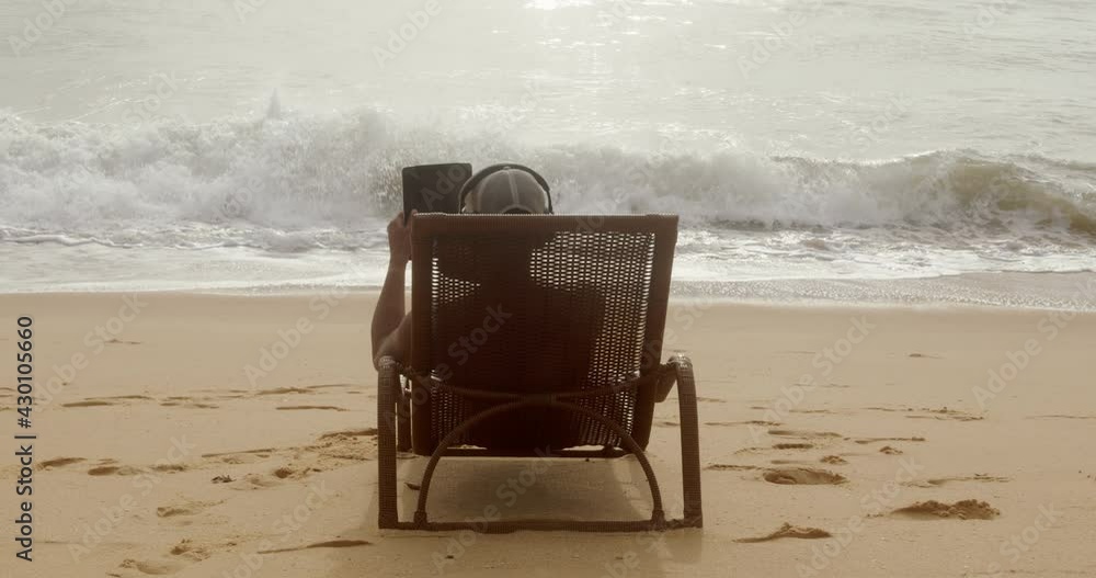 Man making a video call on summer vacation. latin american man sitting on the beach chair with headphones and a tablet Man making a video call on summer vacation. latin american man sitting on the beach chair with headphones and a tablet