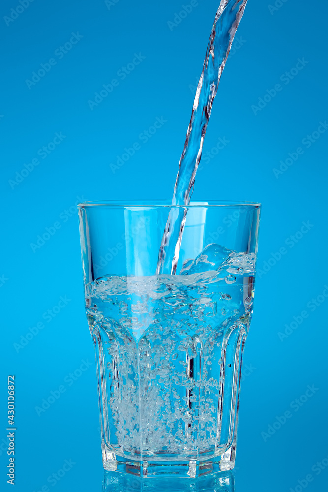 glass cup filled with a stream of fresh drinking water with bubbles and splashes, glassware for drinks glassful on a blue background with a gradient fill. glass cup filled with a stream of fresh drinking water with bubbles and splashes, glassware for drinks glassful on a blue background with a gradient fill.