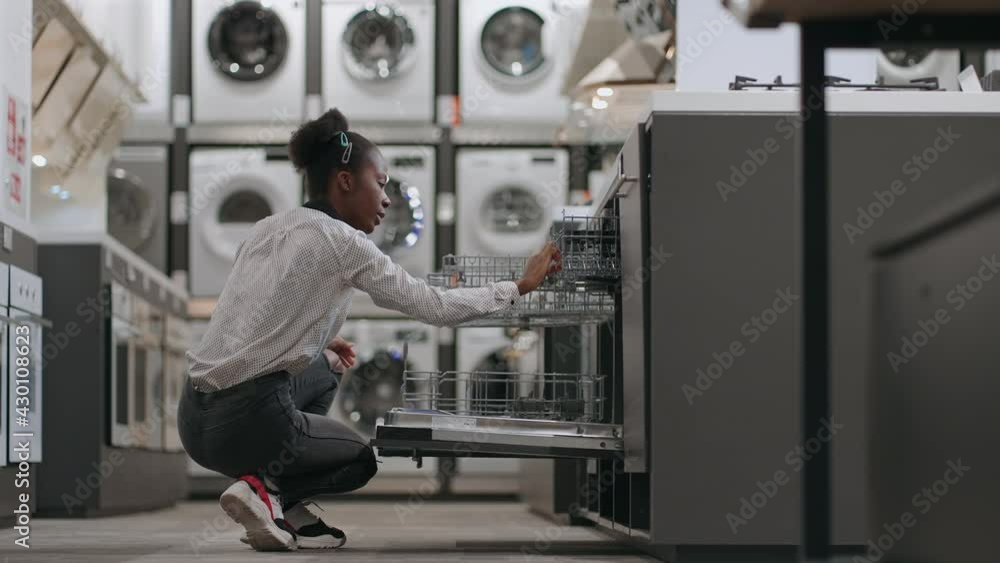 afro-american woman is examining new model of dishwasher in home appliances store, choosing kitchen eqiupment afro-american woman is examining new model of dishwasher in home appliances store, choosing kitchen eqiupment