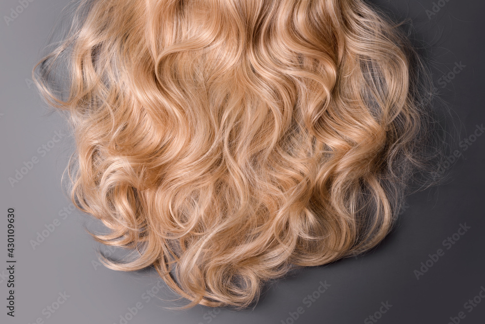 Naklejka premium Blonde hair texture. Wavy long curly blond hair close up as background. Hair extensions, materials and cosmetics, wig, hair care. Hairstyle, haircut or dying in salon.