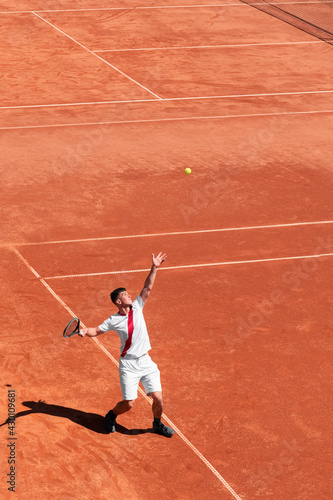 High angle view of young male tennis player performing service on orange clay court at start of match. Individual competition. Vertical sports background, banner, copy space