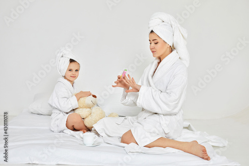 mother making manicure and daughter playing with teddy bear