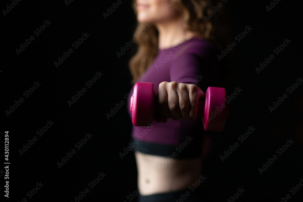 Slim athletic woman on black background in gym. She holding dumbbell in the hand. Close up. Slim athletic woman on black background in gym. She holding dumbbell in the hand. Close up.