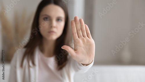 Serious young millennial woman making hand stop gesture at home. Concerned girl showing prohibit, denial signal, palm sign saying no to domestic violence, discrimination, abuse concept. Close up