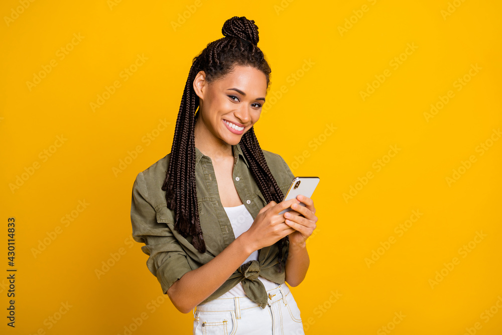 Photo portrait of african american girl holding phone in two hands smiling isolated on vivid yellow colored background Photo portrait of african american girl holding phone in two hands smiling isolated on vivid yellow colored background