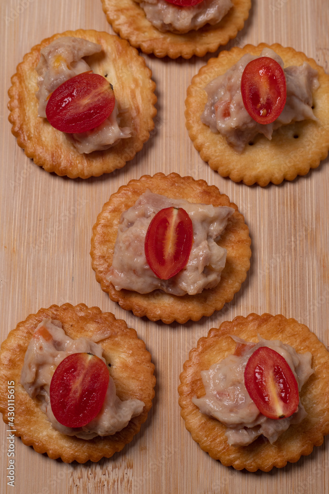 Tuna crackers, bread decorated with tomatoes on a wooden cutting board Copy space