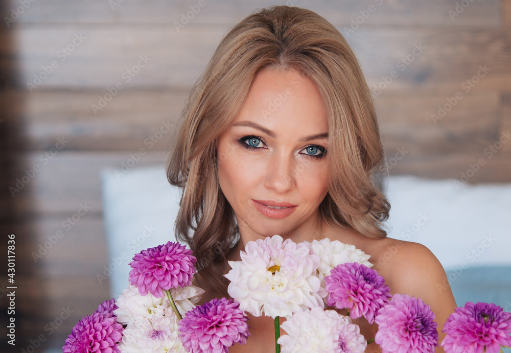 Happy woman with a beautiful smile holding a bouquet of flowers. Peony flowers. Photos taken in the interior. The woman is dressed in a beige top, open shoulders. Happy woman with a beautiful smile holding a bouquet of flowers. Peony flowers. Photos taken in the interior. The woman is dressed in a beige top, open shoulders.