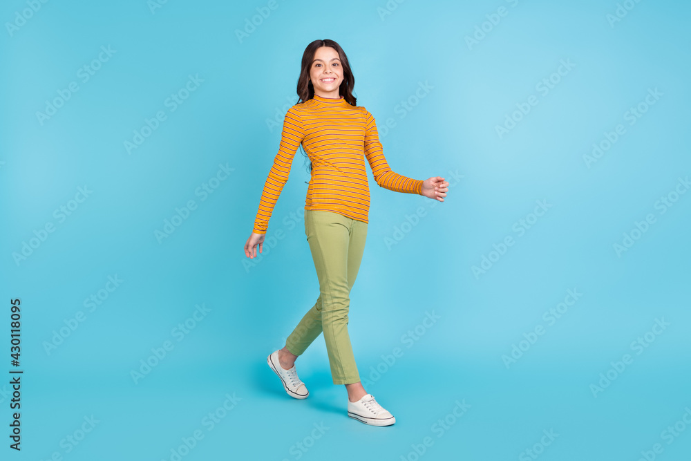 Full body profile portrait of charming cheerful school girl walking toothy smile isolated on blue color background Full body profile portrait of charming cheerful school girl walking toothy smile isolated on blue color background