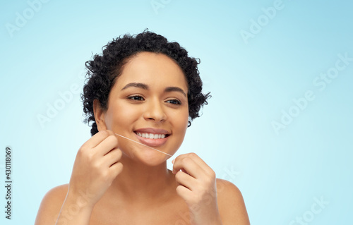 beauty, health and people concept - close up of of happy smiling young african american woman cleaning teeth with dental floss over blue background