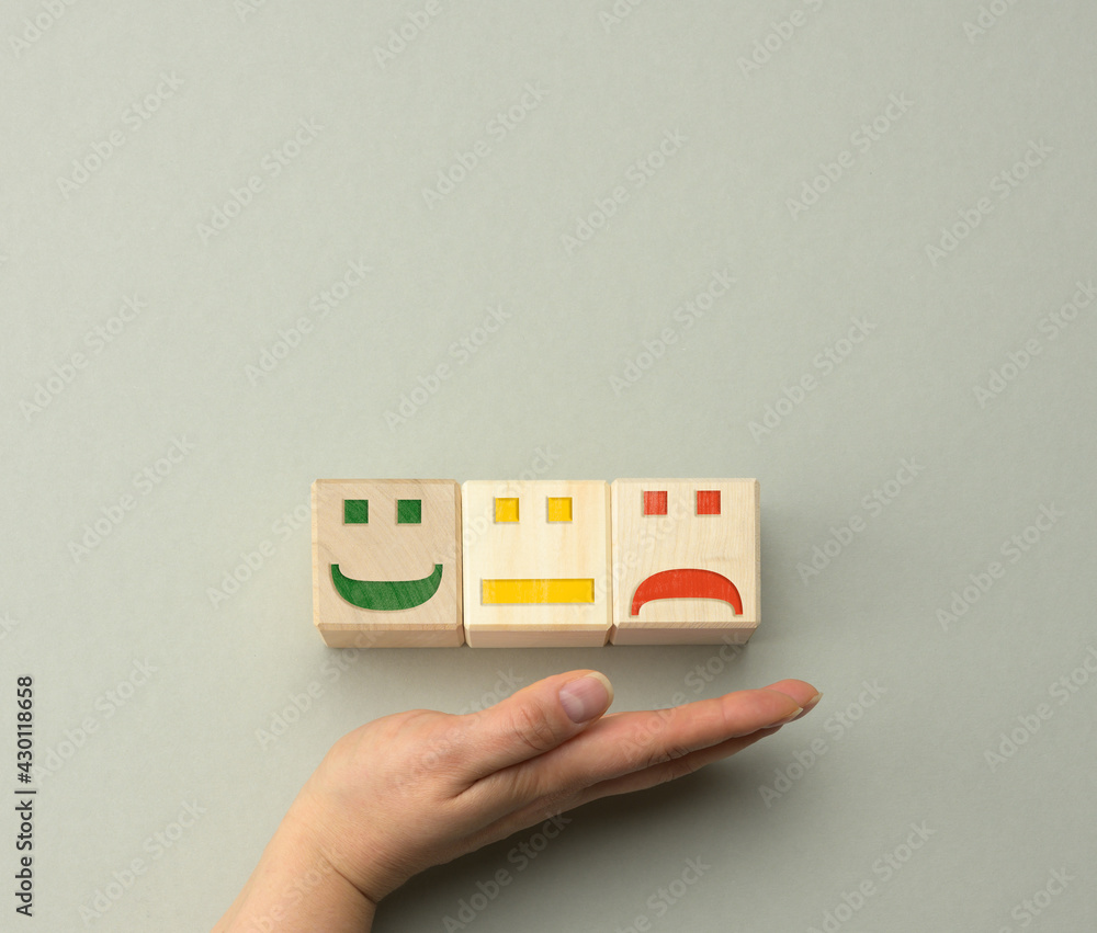 wooden blocks with different emotions from smile to sadness and a woman's hand. concept for assessing the quality of a product or service wooden blocks with different emotions from smile to sadness and a woman's hand. concept for assessing the quality of a product or service