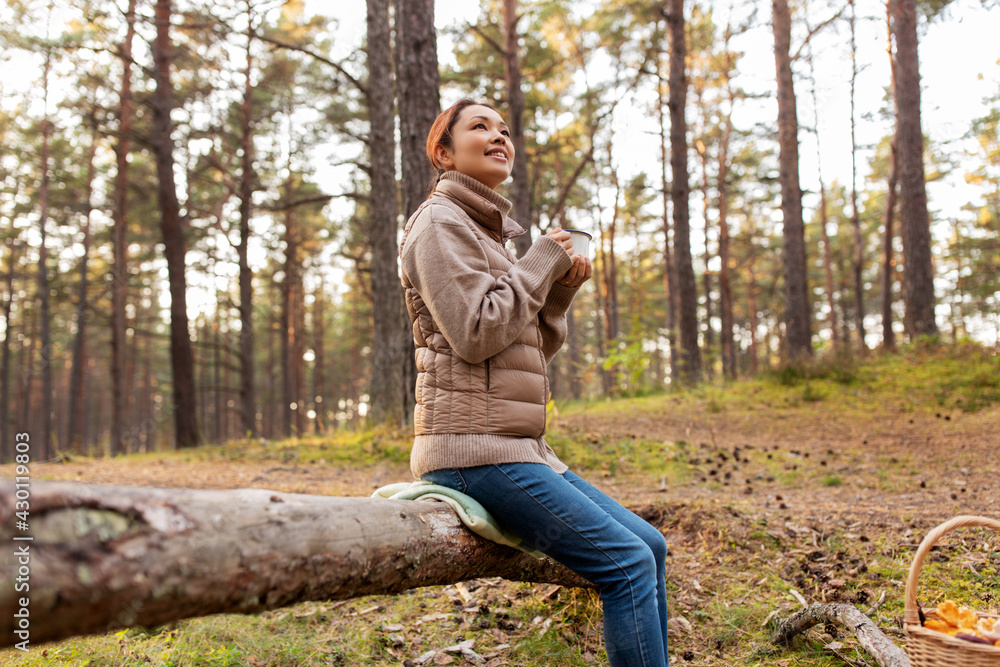 picking season, leisure and people concept - young asian woman with mushrooms in basket drinking tea in autumn forest picking season, leisure and people concept - young asian woman with mushrooms in basket drinking tea in autumn forest