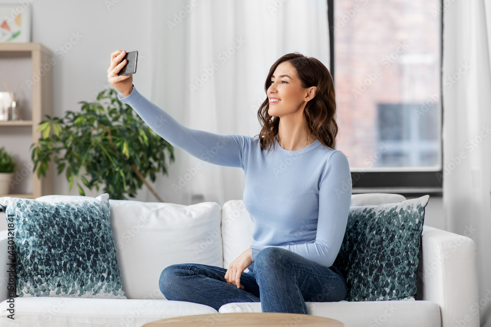 Obraz premium technology and people concept - happy smiling woman with smartphone and taking selfie sitting on sofa at home