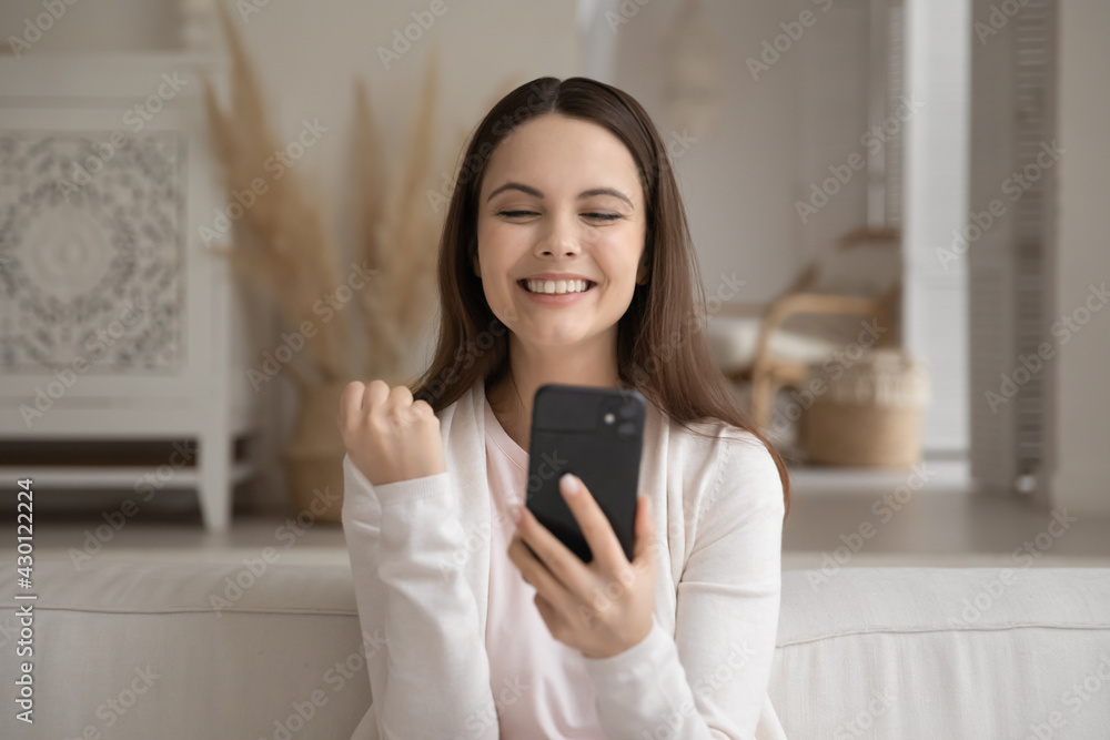 Excited millennial girl with mobile phone feeling joy about good news, making yes winner gesture, celebrating success, reading message on virtual chat about achieve, high result, promotion, win Excited millennial girl with mobile phone feeling joy about good news, making yes winner gesture, celebrating success, reading message on virtual chat about achieve, high result, promotion, win