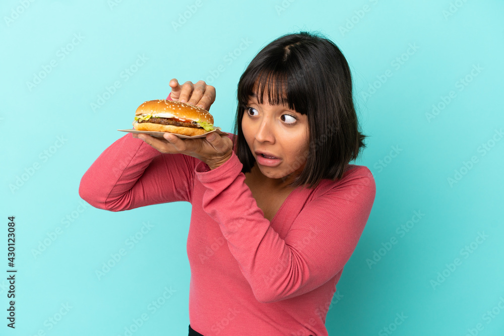Young brunette woman holding a burger over isolated background Young brunette woman holding a burger over isolated background